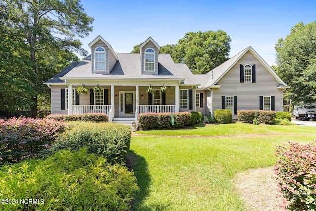 new england style home featuring covered porch, a front yard, and a shingled roof