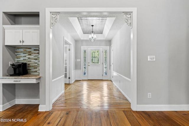 foyer entrance with a textured ceiling, a notable chandelier, parquet flooring, and a tray ceiling