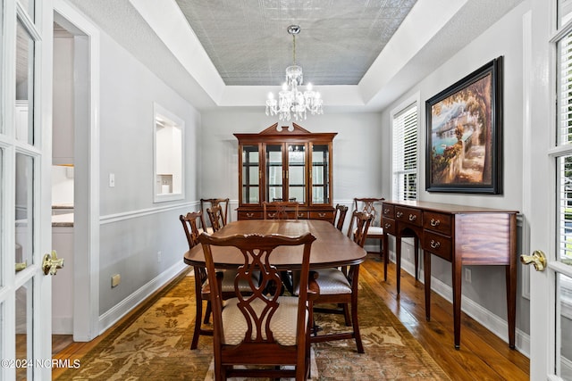 dining room with an inviting chandelier, a raised ceiling, baseboards, and wood-type flooring