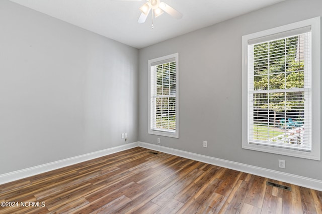 empty room with a wealth of natural light, visible vents, baseboards, and dark wood-style floors