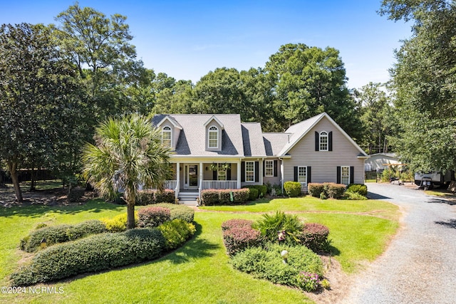 new england style home featuring gravel driveway, a front lawn, and covered porch