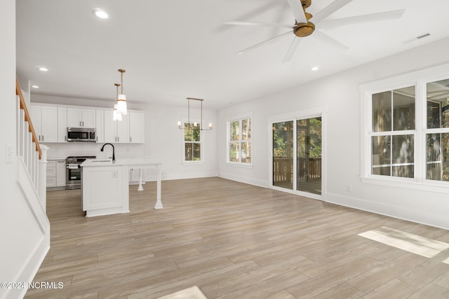 interior space with appliances with stainless steel finishes, ceiling fan with notable chandelier, a kitchen island with sink, decorative light fixtures, and white cabinets