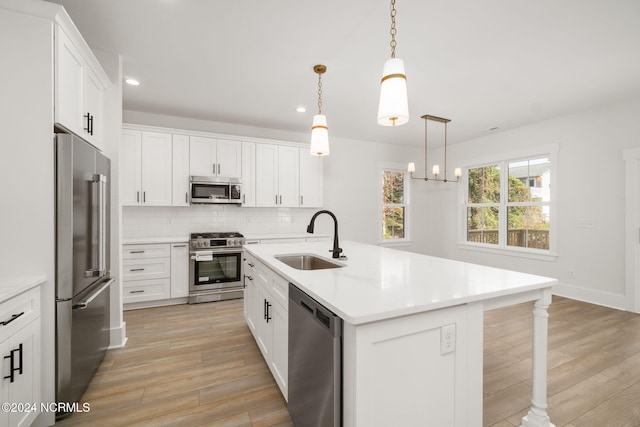 kitchen with stainless steel appliances, sink, white cabinetry, hanging light fixtures, and an island with sink