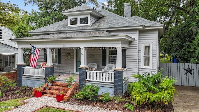 view of front of home featuring a porch, fence, a shingled roof, and a chimney