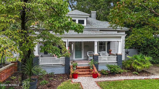 view of front of house with a shingled roof, covered porch, fence, and a chimney