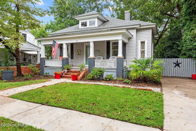 bungalow-style house featuring a porch, fence, a front lawn, a chimney, and a shingled roof