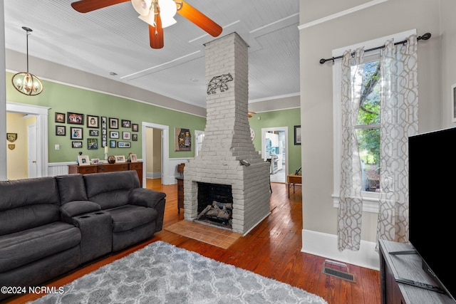 living room featuring ceiling fan with notable chandelier, a fireplace, ornamental molding, and dark wood-type flooring