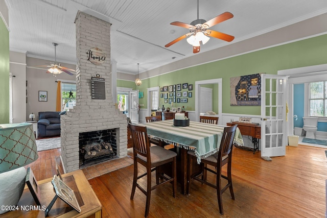 dining area with a wealth of natural light, a fireplace, wood-type flooring, and a ceiling fan