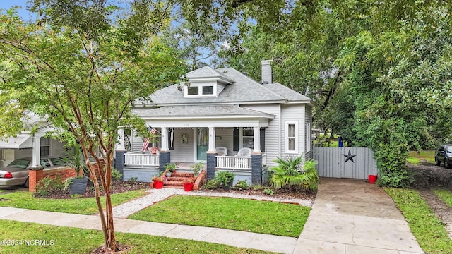 bungalow featuring concrete driveway, a chimney, a gate, a shingled roof, and covered porch