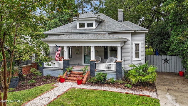 bungalow-style home featuring a porch, a chimney, a shingled roof, and fence