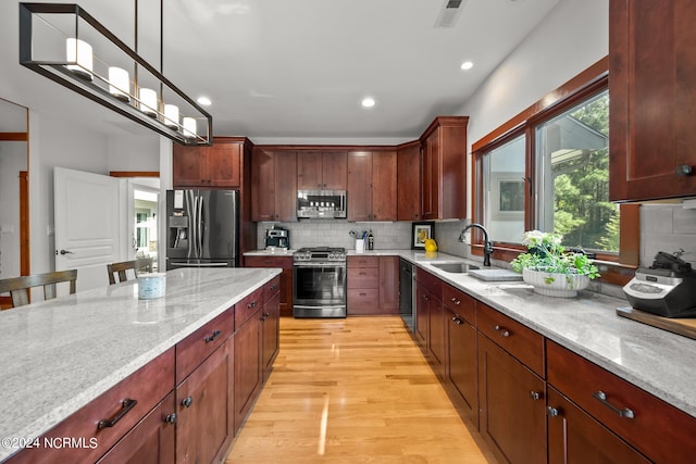 kitchen with decorative light fixtures, light hardwood / wood-style floors, stainless steel appliances, sink, and decorative backsplash