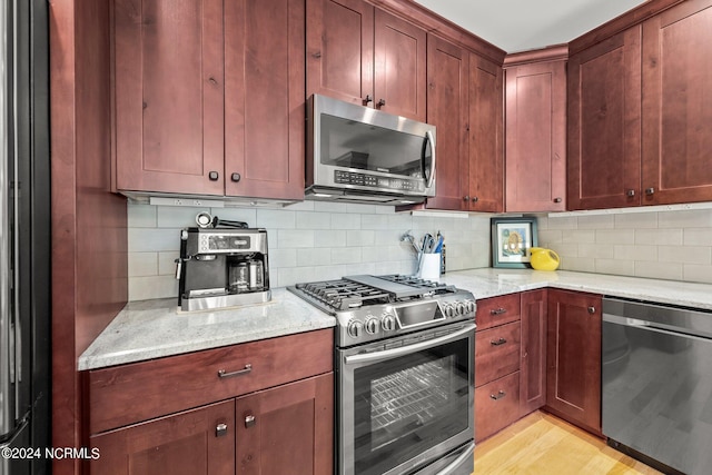 kitchen with light wood-type flooring, appliances with stainless steel finishes, light stone counters, and decorative backsplash