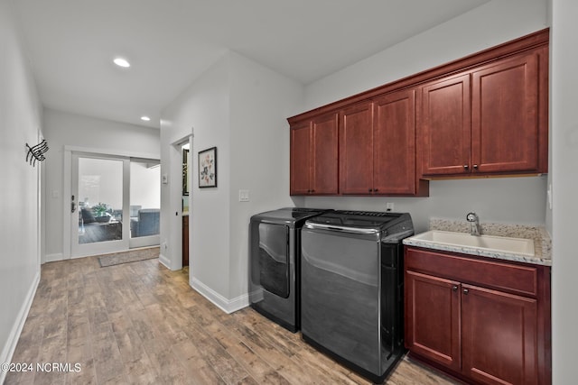 laundry room with washing machine and clothes dryer, cabinets, sink, and light hardwood / wood-style floors