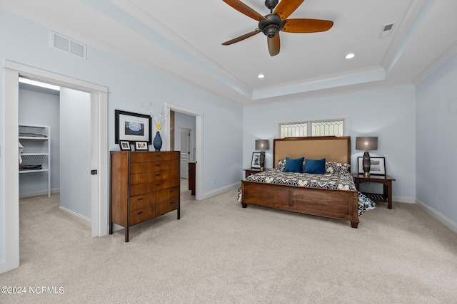 bedroom with a raised ceiling, ceiling fan, a spacious closet, and light colored carpet