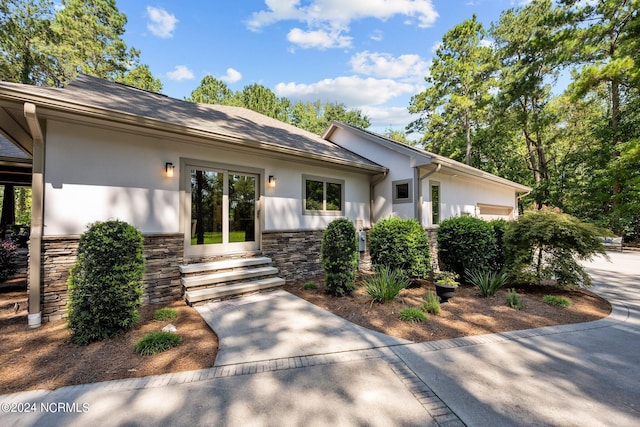 view of front of home featuring a garage, stone siding, entry steps, and stucco siding