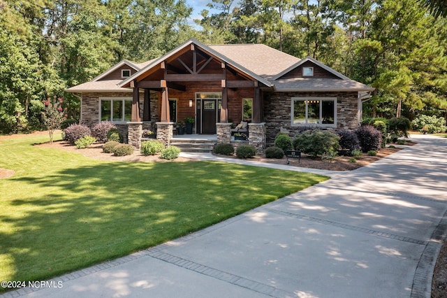 craftsman inspired home with stone siding, covered porch, a front lawn, and roof with shingles