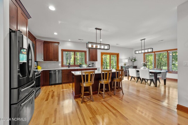 kitchen featuring decorative light fixtures, light hardwood / wood-style flooring, appliances with stainless steel finishes, a center island, and decorative backsplash