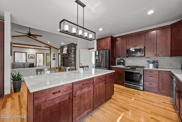 kitchen featuring vaulted ceiling, light hardwood / wood-style flooring, a stone fireplace, tasteful backsplash, and stainless steel appliances