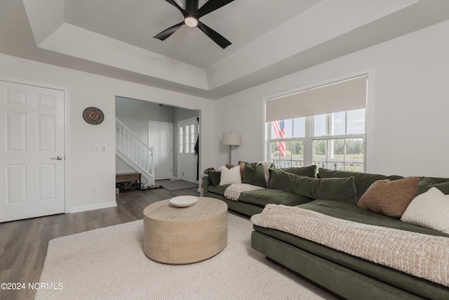 living area featuring baseboards, a raised ceiling, ceiling fan, wood finished floors, and stairs