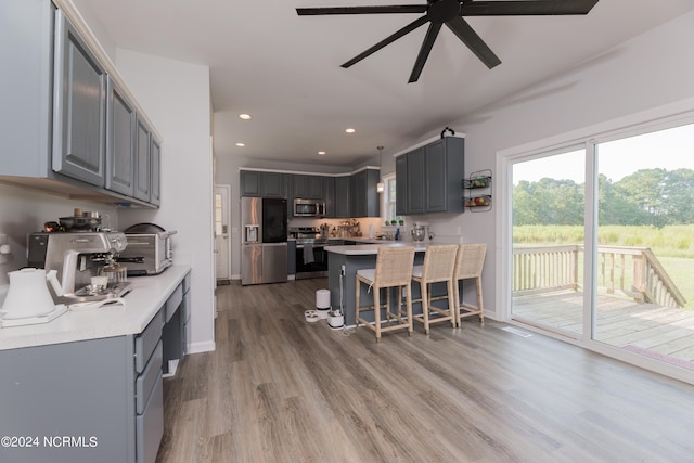 kitchen with ceiling fan, gray cabinets, appliances with stainless steel finishes, a breakfast bar area, and light wood-type flooring