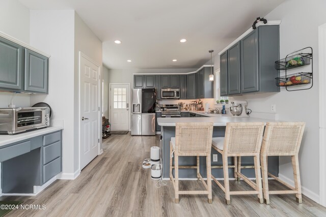 kitchen featuring kitchen peninsula, pendant lighting, stainless steel appliances, light wood-type flooring, and a kitchen bar