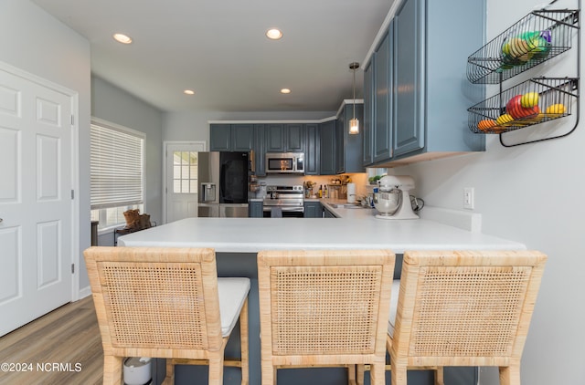 kitchen with blue cabinets, hardwood / wood-style floors, kitchen peninsula, stainless steel appliances, and a kitchen bar