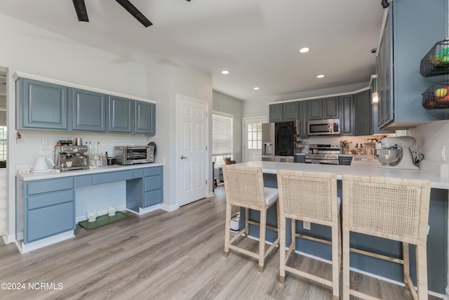 kitchen with ceiling fan, kitchen peninsula, light hardwood / wood-style flooring, stainless steel appliances, and a breakfast bar area