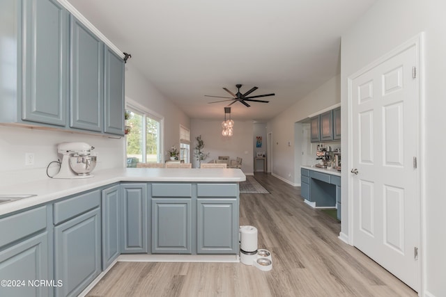 kitchen with a peninsula, a ceiling fan, hanging light fixtures, light countertops, and light wood finished floors