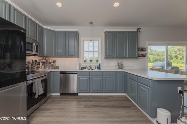 kitchen with kitchen peninsula, pendant lighting, stainless steel appliances, light wood-type flooring, and sink