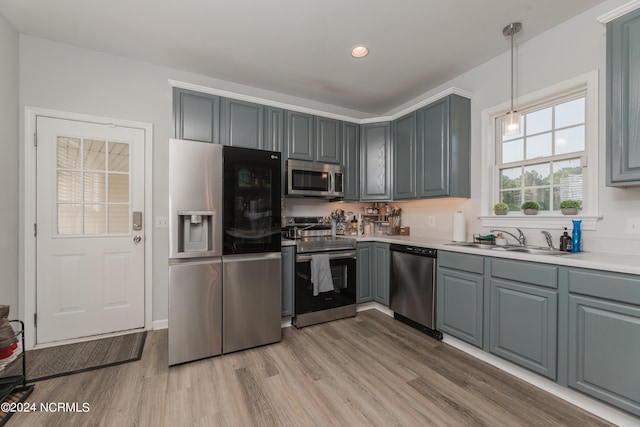 kitchen featuring light wood-style flooring, a sink, light countertops, appliances with stainless steel finishes, and hanging light fixtures