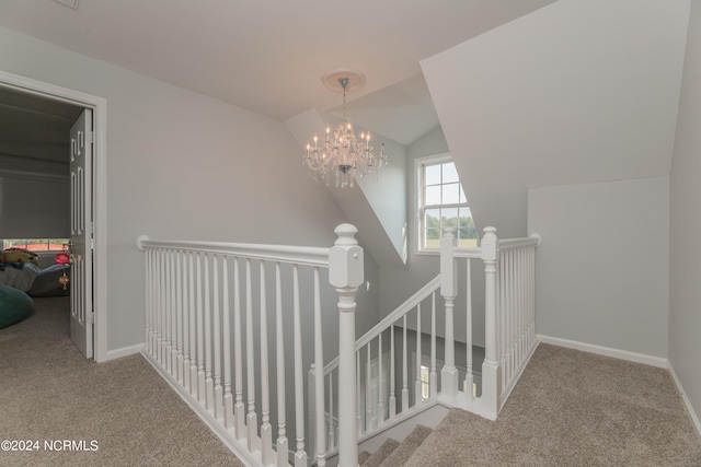 hall featuring lofted ceiling, a chandelier, carpet flooring, an upstairs landing, and baseboards