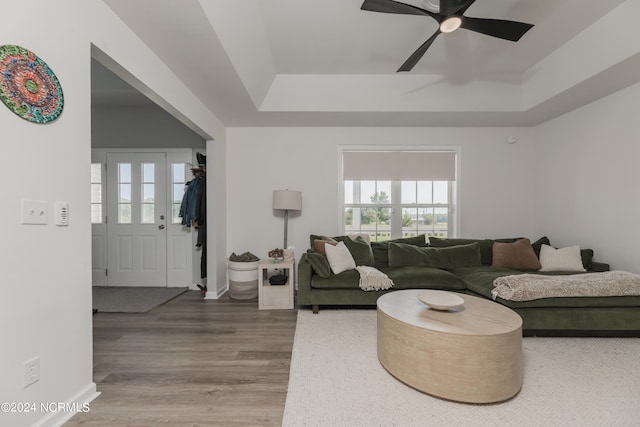 living room with a tray ceiling, wood finished floors, a ceiling fan, and baseboards