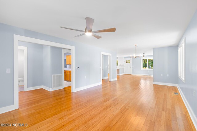 unfurnished living room with ceiling fan with notable chandelier and light wood-type flooring