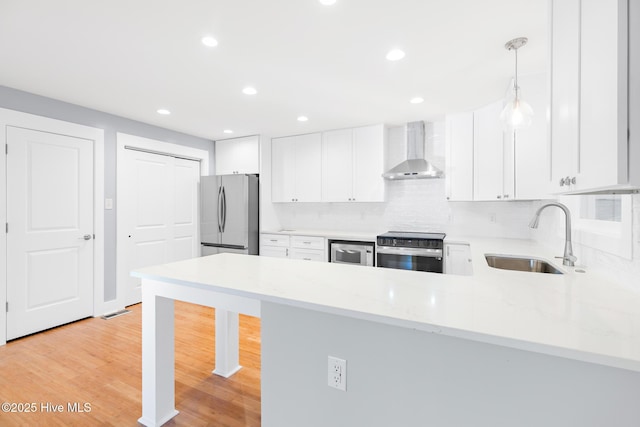 kitchen featuring wall chimney exhaust hood, sink, decorative light fixtures, stainless steel appliances, and white cabinets