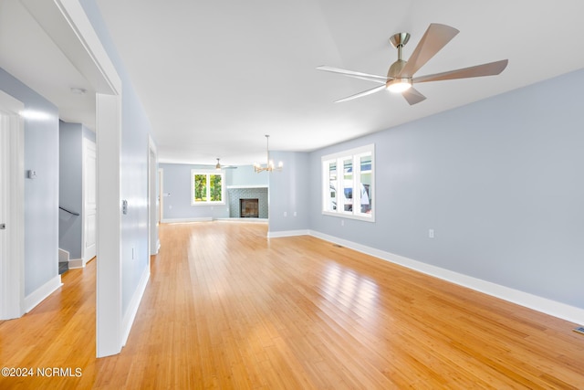31 Augusta Dr, Oak Island, NC 28465 - unfurnished living room with baseboards, light wood-type flooring, a fireplace with raised hearth, and ceiling fan with notable chandelier