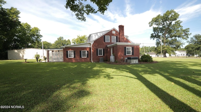 back of property featuring a yard, brick siding, a chimney, and central AC unit