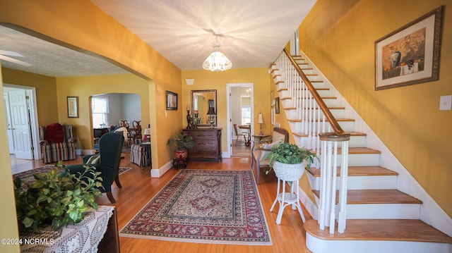 foyer with baseboards, arched walkways, stairway, wood finished floors, and a textured ceiling