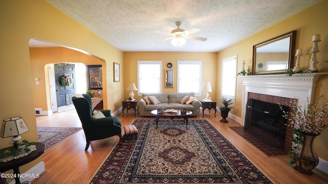 living room featuring a textured ceiling, arched walkways, wood finished floors, and a tile fireplace