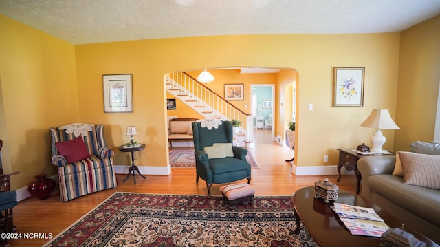 living area with arched walkways, stairway, a textured ceiling, and wood finished floors