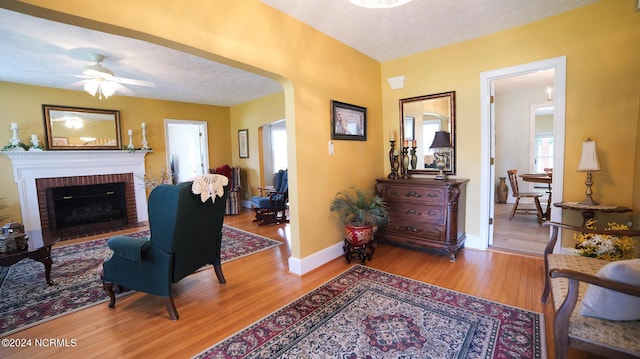 living area featuring baseboards, arched walkways, wood finished floors, a textured ceiling, and a fireplace