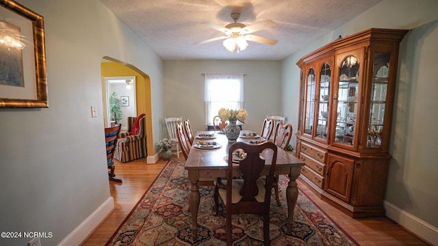 dining space with light wood-style flooring, arched walkways, ceiling fan, and a textured ceiling