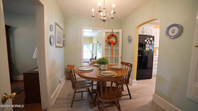 dining space featuring arched walkways, a notable chandelier, vaulted ceiling, light wood-type flooring, and baseboards