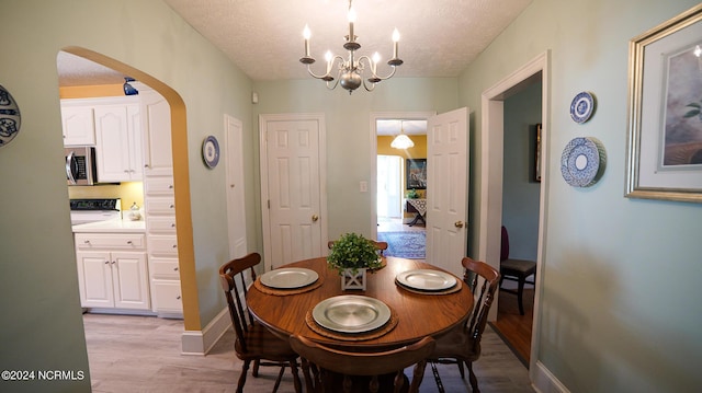 dining room with arched walkways, baseboards, a textured ceiling, and light wood finished floors