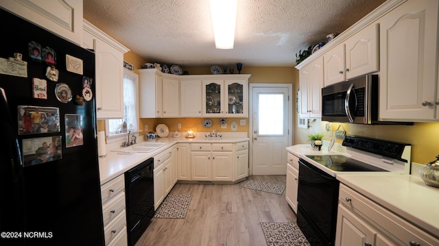 kitchen with light wood finished floors, light countertops, white cabinetry, a sink, and black appliances