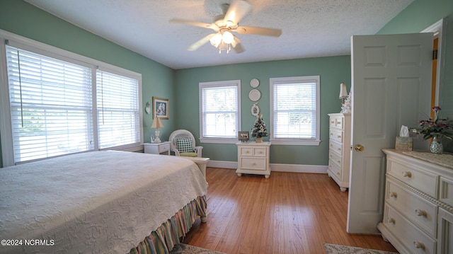 bedroom with light wood-type flooring, ceiling fan, baseboards, and a textured ceiling