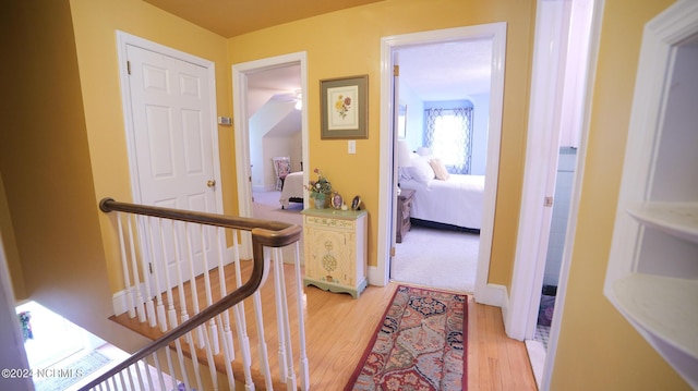 hall with light wood-type flooring, an upstairs landing, and baseboards