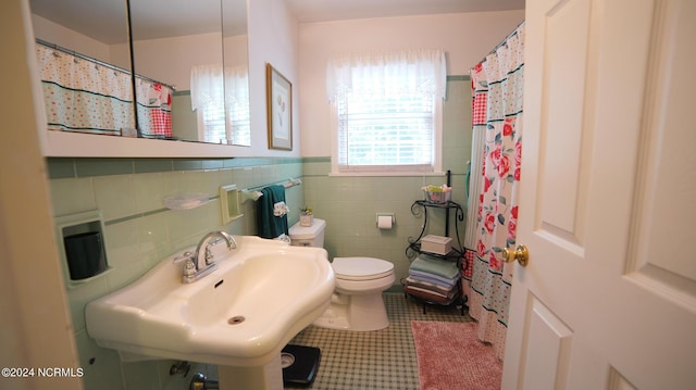 bathroom with tile walls, toilet, wainscoting, a sink, and tile patterned flooring