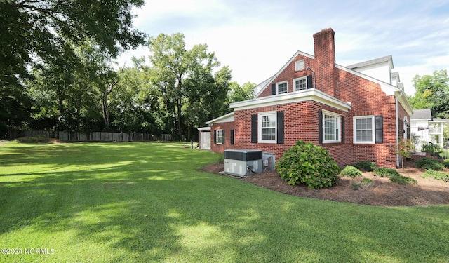 view of home's exterior featuring brick siding, a yard, a chimney, fence, and cooling unit