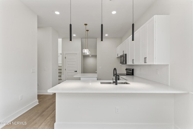 kitchen with kitchen peninsula, hanging light fixtures, light wood-type flooring, sink, and stainless steel appliances