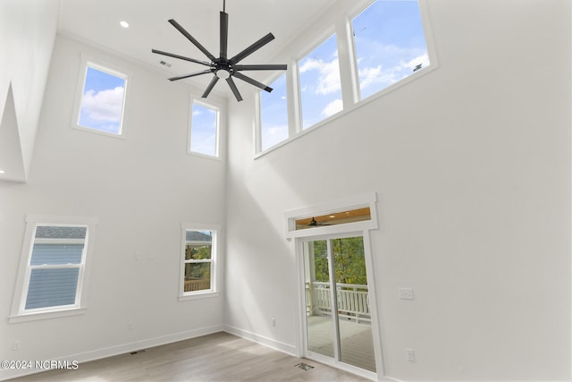 unfurnished living room featuring ceiling fan, a high ceiling, and light wood-type flooring